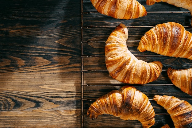 Croissants on a baking rack cool after baking on a dark wooden table