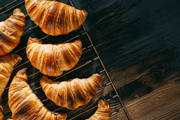 Croissants on a baking rack cool after baking on a dark wooden table