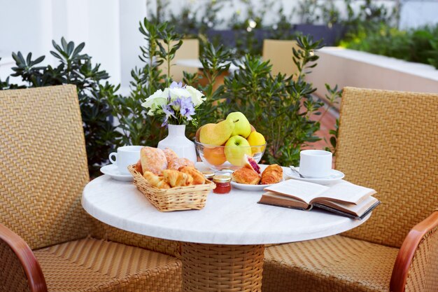 Croissants, fruit, koffie, jam en een boek worden op de ontbijttafel op het terras gelegd