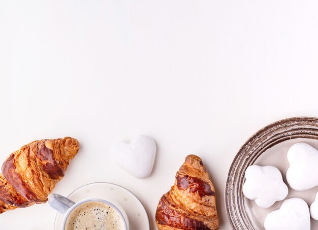 Cornetti, biscotti glassati e una tazza di caffè su un tavolo di legno bianco. mattina natura morta. vista dall'alto con spazio di copia per il testo.