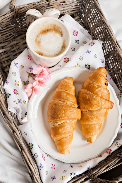 Croissants koffiekopje bloem in romantische stijl op een rieten dienblad op wit beddengoed