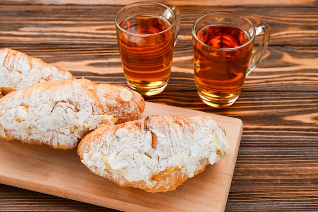 Croissants met amandelen en thee op een houten tafel.