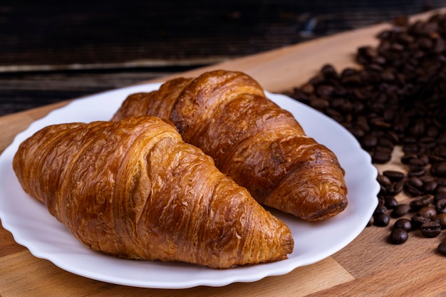 Foto croissants op een witte plaat en koffiebonen op een houten bord