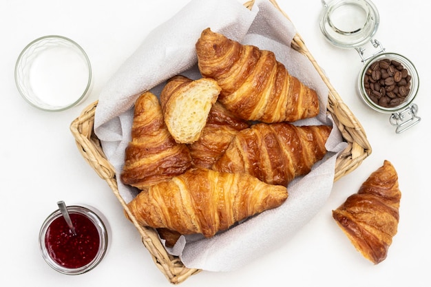 Croissants in wicker basket. Grains of coffee in jar, cream in glass. Flat lay.  White background.