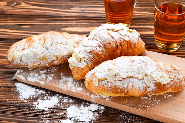 Croissants with almonds and tea on a wooden table.