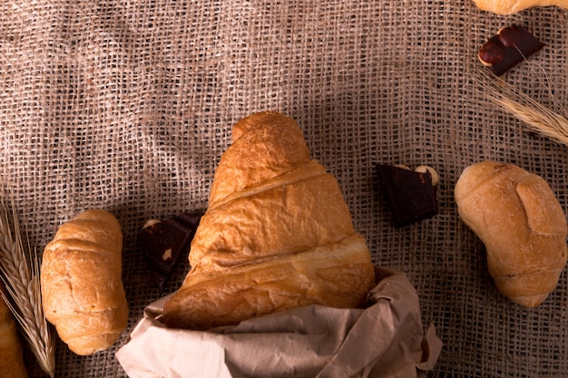 Croissants with chocolate on board near wheat on sackcloth background. Rustic style. Top view.