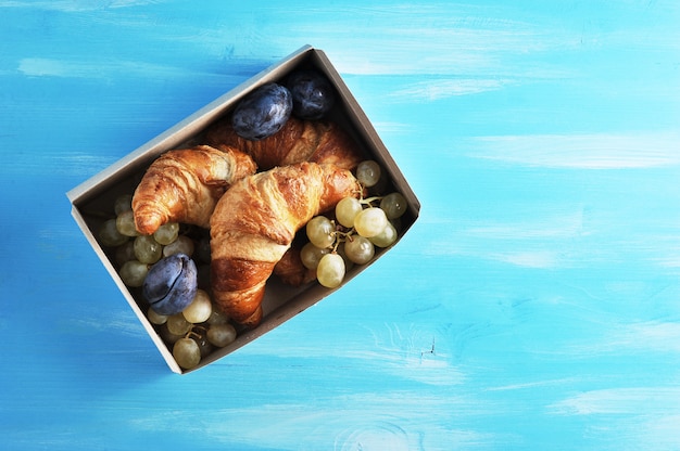 Croissant con frutta in una scatola su un blu di legno