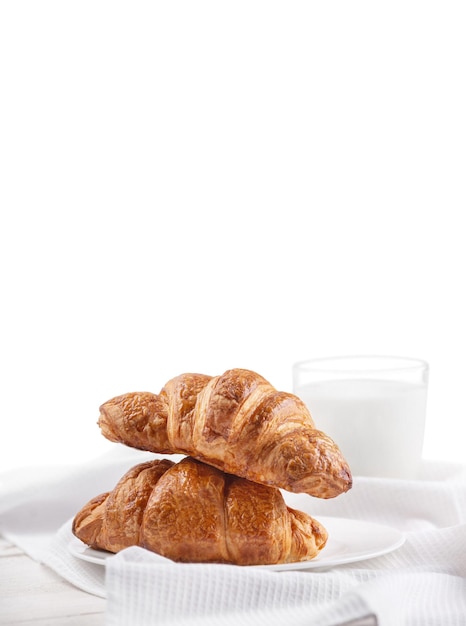 Croissant con un bicchiere di latte su un fondo di legno bianco