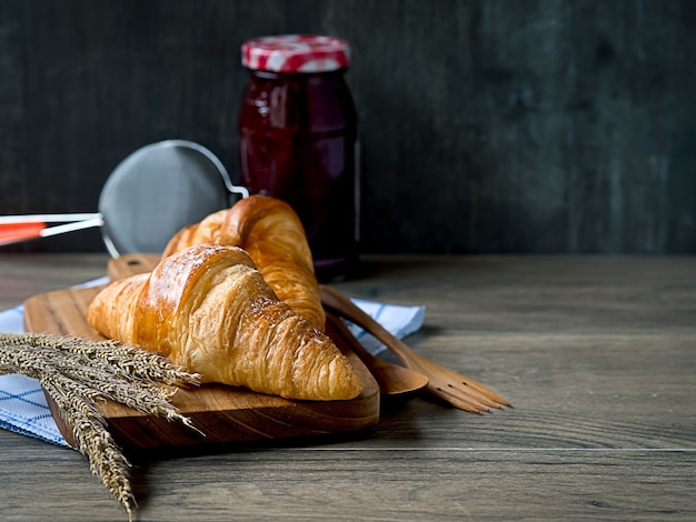 Photo croissants on the wooden board with strawberry jam jar and strainer on wooden table