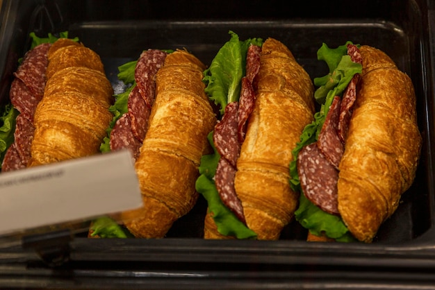 Croissantsandwiches gevuld met salami en kruiden op de toonbank in de winkel ongezond fastfood close-up