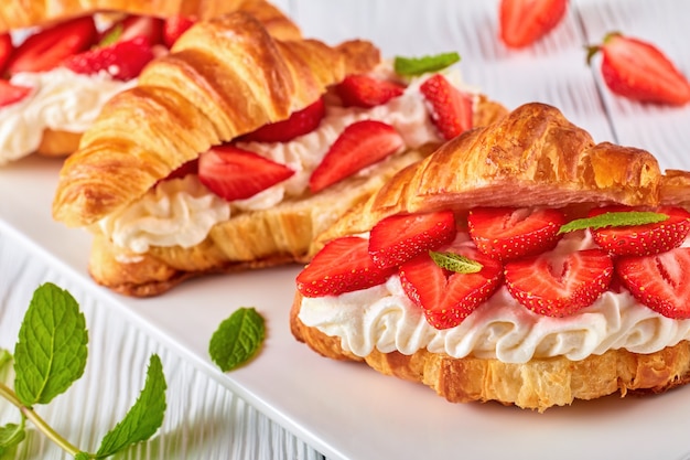 Croissantsandwiches met verse rijpe aardbeien en slagroomkaas op een schotel op witte houten lijst