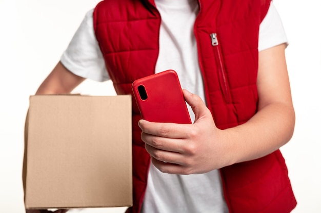 Photo crop anonymous delivery man in red uniform scanning carton box with mobile phone while delivering parcel