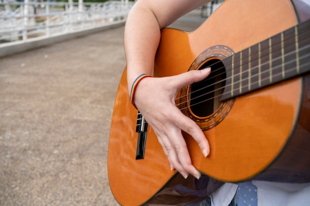 写真 都市の通りで歌を演奏しながらアコースティックギターを演奏するlgbt腕輪を身に着けた匿名の女性ギタリスト