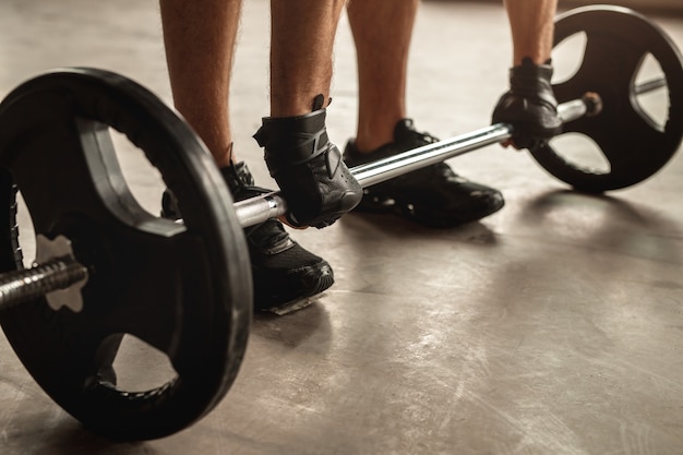 Ritaglia lo sportivo anonimo in guanti che si piega in avanti mentre si prepara a sollevare un bilanciere pesante durante l'allenamento con i pesi in palestra