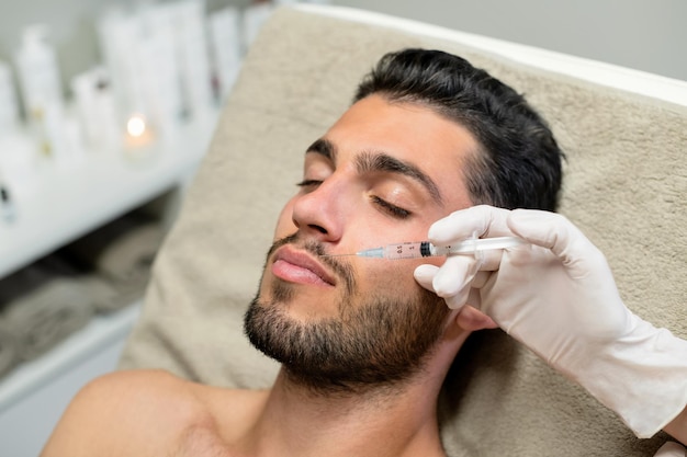 Crop beautician injecting filler into lips of customer