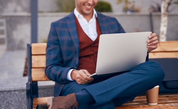 Crop businessman using laptop on bench