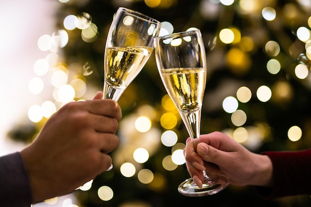 Crop close up of man and woman hold glasses with champagne clink greet congratulate with New Year Couple celebrate Christmas winter holidays at home together wish luck and joy Celebration concept