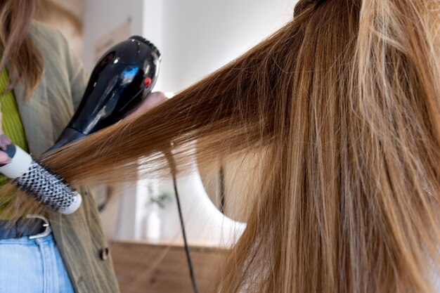 Crop hairdresser blow drying hair of client