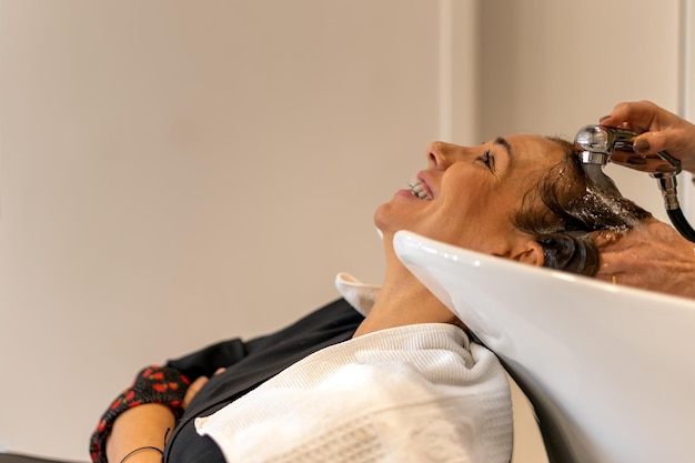 Crop hairdresser washing hair of smiling client using tap