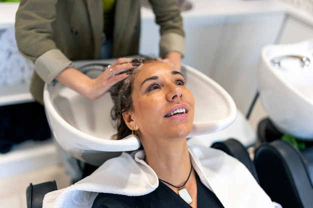 Crop hairstylist washing hair of client in sink