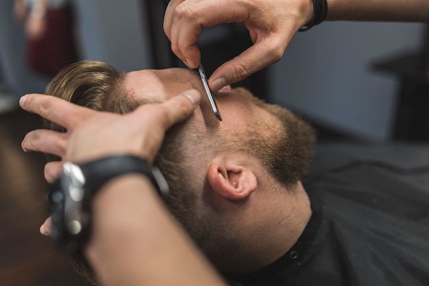 Crop hands shaving bearded man