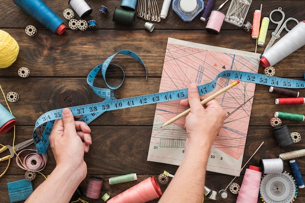 Crop hands with tape measure near sewing stuff