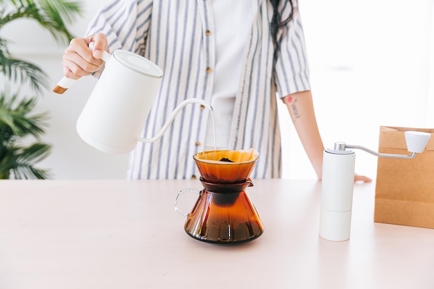 写真 ガラスのドリッパーのペーパーフィルターの上に挽いたコーヒーに熱湯を注ぐ黒い長い髪の手を持つプロの女性バリスタのトリミング画像別の方法は滴下と呼ばれています