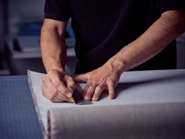 Crop male bookbinder making marks on paper while using pencil and ruler and working at workbench in workshop