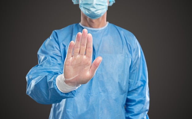 Crop male doctor in protective suit making stop gesture during covid