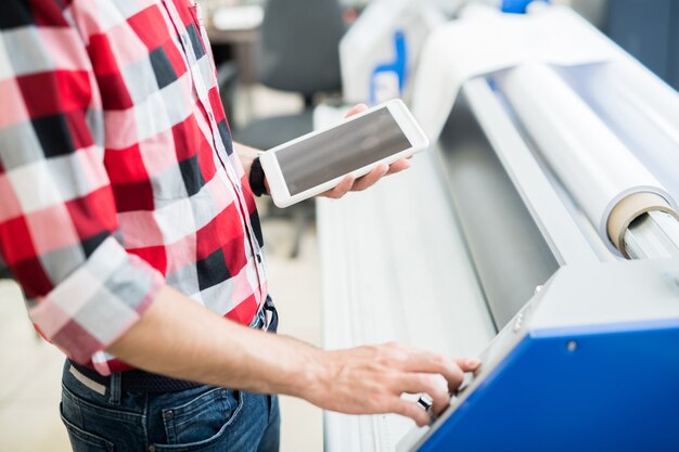 Crop man with tablet using printing equipment