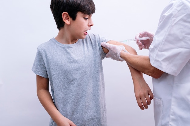 Infermiera del raccolto in guanti di lattice bianco che tiene la spalla del ragazzo con i capelli ricci mentre fa l'iniezione del vaccino