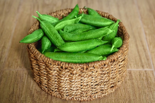 The crop of peas lies in a round wicker basket on a wooden background. central composition.