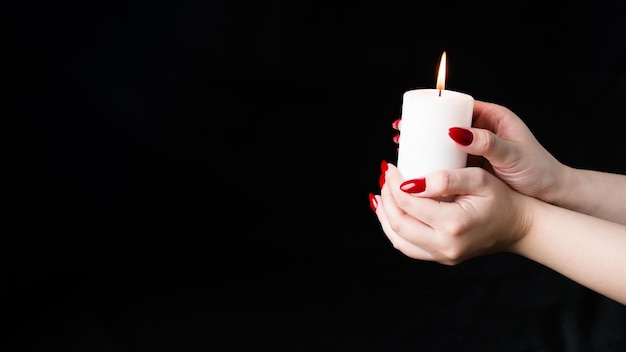 Crop person with burning candle Crop anonymous person demonstrating white candle black background