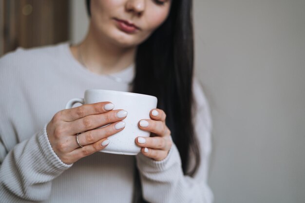 Crop photo of beautiful smiling woman teenager girl with dark
long hair in home clothes with the morning cup of coffee