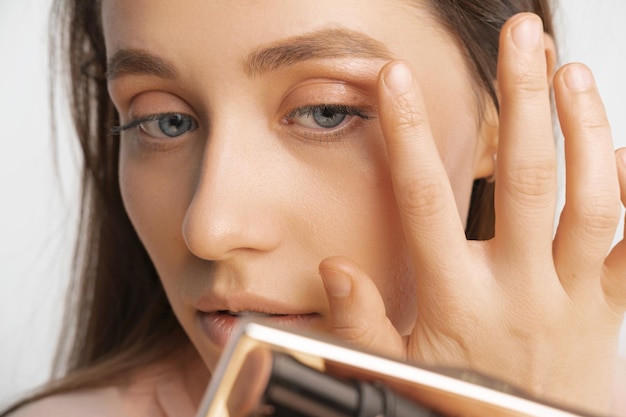 Photo crop photo of a young woman touching face while applying makeup