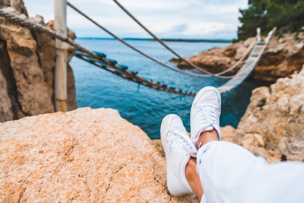 Crop picture woman legs at cliff suspension bridge on background