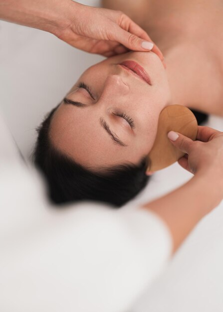 Crop professional cosmetician using gua sha tool during face massage