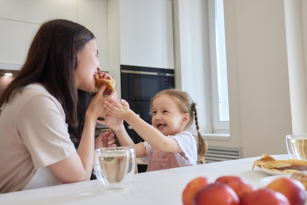 빨간 옷을 입은 어머니와 부엌에 앉아 있는 다채로운 도넛을 먹는 딸의 자르기 다이어트 개념과 정크 푸드