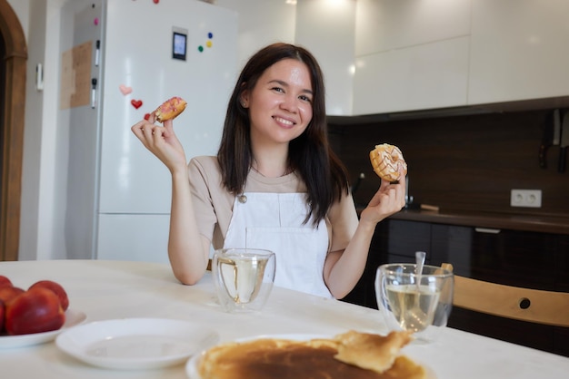 赤い服を着た母親と娘が台所に座ってカラフルなドーナツを食べているクロップショットダイエットのコンセプトとジャンクフード