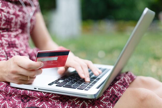 Кадрированный снимок женщины в платье с ноутбуком и кредитной картой для покупок во время отдыха в парке