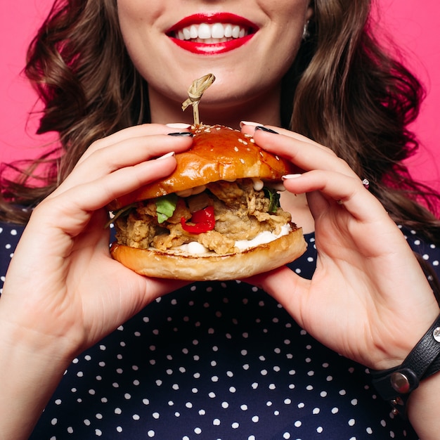 Crop of smiling woman with red lips holding juicy burger.