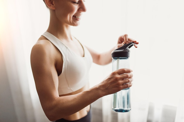 Crop sportswoman opening bottle of water