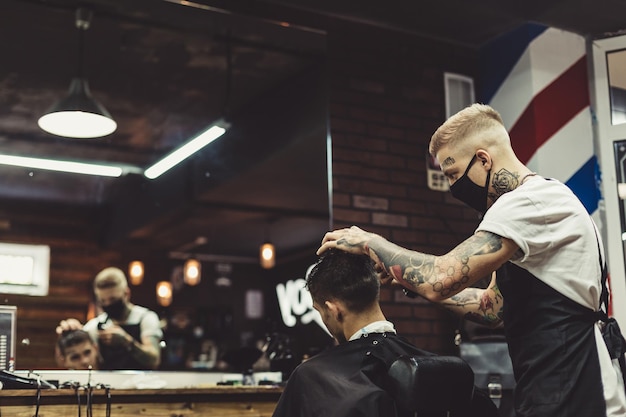 Татуированный стилист сосредоточился на бритье мужчины с машинкой, делающей прическу