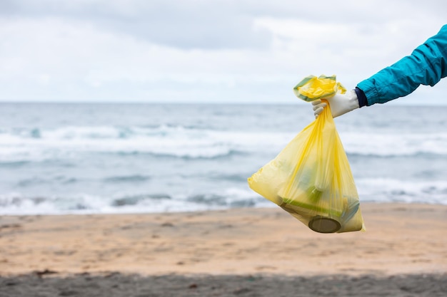 Crop unrecognizable female activist showing bag with collected garbage on seashore