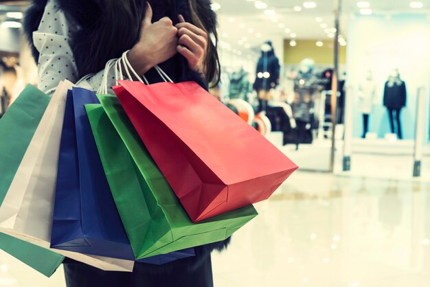 Crop unrecognizable girl clasping many shopping bags on mall background Lady making many purchases in store Concept of female incidentals Looking for discount things black Friday Designer mockup