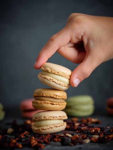 Crop unrecognizable kid putting sweet tasty macaroons on top of each other placed on table with dried fruit tea leaves