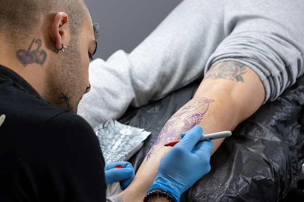 Crop of unrecognizable professional artist tattooist making marks on client's leg before making a tattoo in his tattoo studio