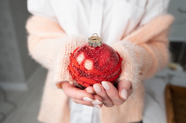 手に赤いクリスマスの光沢のあるボールを保持している女性の作物ビュー。休日の準備。居心地の良い冬。高品質の写真