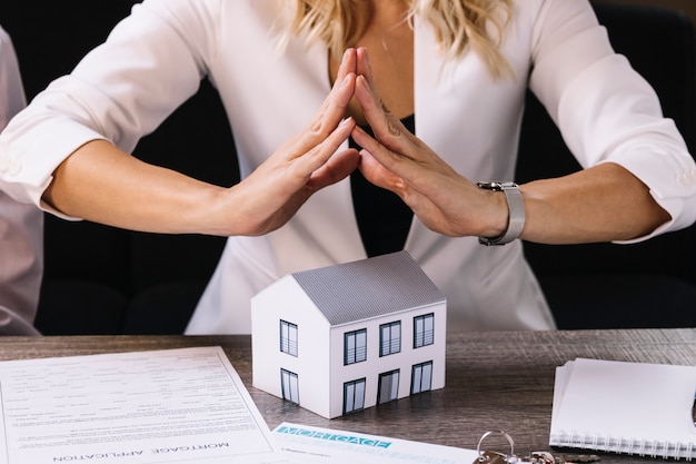 crop woman holding hands above toy house