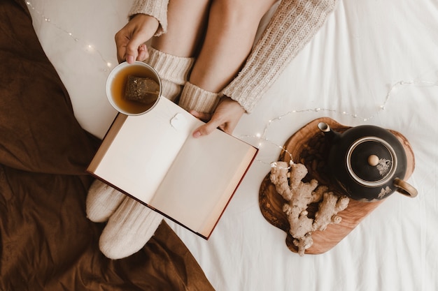 Crop woman reading and drinking near ginger